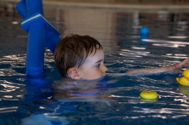 Havuzda yüzme cihazları kullanan, renkli oyuncaklarla uğraşan, yüzme ve su güvenliğine odaklanan küçük bir çocuk