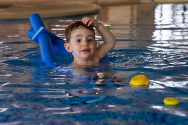 Küçük çocuk yüzme derslerinden, yüzen oyuncaklarla oynamaktan ve havuzda temel su güvenliği becerilerini öğrenmekten hoşlanıyor.