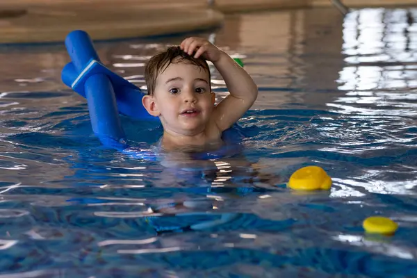 Küçük çocuk yüzme derslerinden, yüzen oyuncaklarla oynamaktan ve havuzda temel su güvenliği becerilerini öğrenmekten hoşlanıyor.