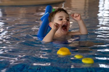 Küçük çocuk yüzme dersleri almaktan, yüzen oyuncaklarla oynamaktan ve havuzda yüzme aleti kullanmaktan hoşlanıyor.