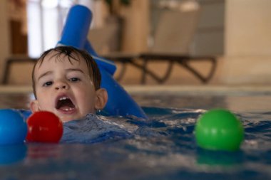 Küçük çocuk yüzme dersleri almaktan, yüzme aleti kullanmaktan ve kapalı havuzda renkli toplarla oynamaktan hoşlanıyor.