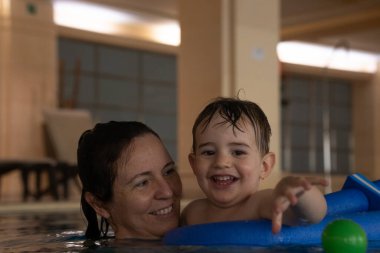 Mutlu anne ve oğul birlikte vakit geçiriyorlar, kapalı havuzda şişme oyuncaklarla oynuyorlar, bağ kurmayı ve eğlenmeyi teşvik ediyorlar.