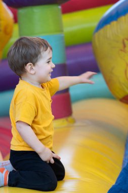 Genç bir çocuk renkli şişme bir kalede diz çöküp eğleniyor, bir topla oynamak için uzanıyor.