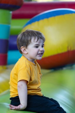 Anaokulu öğrencisi renkli şişme bir şatoda oynayıp zıplıyor, güneşli bir günün tadını çıkarıyor.