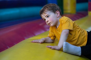 Renkli bir şişme şatoda sürünen genç bir çocuk lunaparkta oyun oynamanın tadını çıkarıyor.