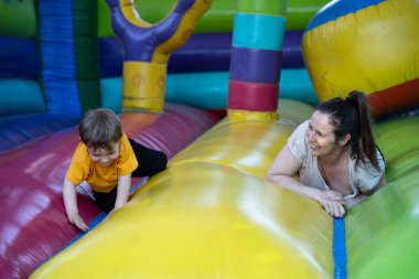 Mutlu anne ve oğul renkli şişme bir şatoda emekliyor ve birlikte oynuyorlar. Birlikte güzel vakit geçiriyorlar.