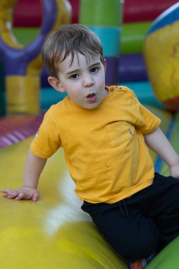 Heyecanlı çocuk, renkli şişme bir şatoda oynayan, oyun parkında güneşli bir günün tadını çıkaran.