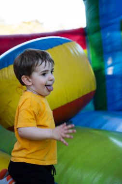 Şişme şişme bir evde hoplayıp zıplarken dilini çıkaran sarı tişörtlü genç çocuk.