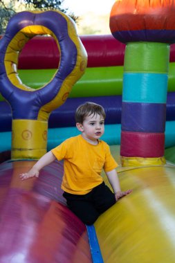 Genç bir çocuk güneşli bir günün tadını çıkarıyor, açık hava oyun sahasında renkli bir şatoda oynuyor.