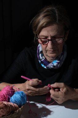 Pembe iplikle ustalıkla örgü ören, loş bir ortamda karmaşık dikişler atan, geleneksel bir zanaat sergileyen son sınıf öğrencisi kadın.