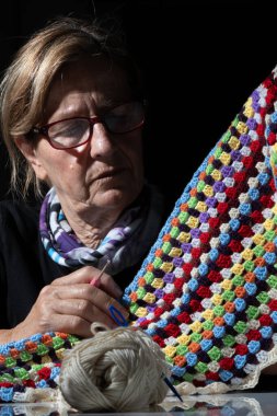 Konsantre olmuş yaşlı bir zanaatkar enerjik bir örgü örüyor, iplik ve kancayla ustalıkla çalışıyor.