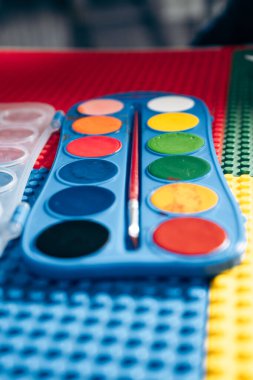 Renkli bir oyun hasırının üzerinde dinlenen canlı bir suluboya paleti, oyuncu bir yaratıcılık ve sanatsal ifade hissi uyandırır.