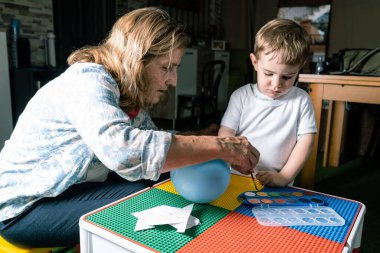 Büyükanne ve torun neşeyle suluboya ile renkli bir balon çiziyorlar, küçük bir masada birlikte oturuyorlar, yaratıcılığı teşvik ediyorlar ve bağ kuruyorlar.