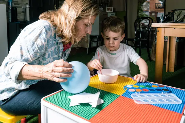 Büyükanne ve torun yaratıcı oyun zamanlarını seviyorlar, evde suluboya bir balon çiziyorlar, aile bağlarını ve sanatsal ifadeyi destekliyorlar.