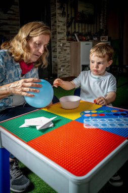 Büyükannem ve torunum evde suluboya bir balon boyuyor, renkli masalarda oturuyorlar.