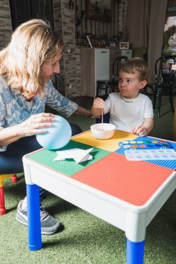Büyükanne ve torun birlikte yaratıcı zaman geçiriyorlar, renkli bir masada balon boyuyorlar.