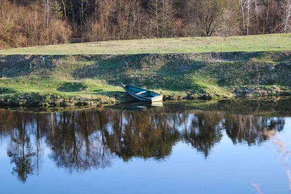 Sakin nehrin kenarında dinlenen bir tekne etrafındaki ağaçları yansıtıyor..
