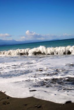 Dalgaları, denizi ve mavi gökyüzü olan güzel sahil.