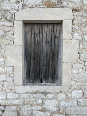 Eski gri ahşap tahtalar beyaz taşla çerçevelenmiş küçük bir pencereyi tamamen kapatıyor. Dokular, arka planlar ya da tasarım referansları için mükemmel
