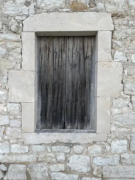 Eski gri ahşap tahtalar beyaz taşla çerçevelenmiş küçük bir pencereyi tamamen kapatıyor. Dokular, arka planlar ya da tasarım referansları için mükemmel