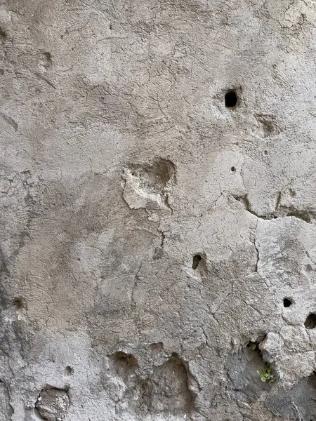 Görünür çatlaklar, delikler ve desenli sıva içeren kabataslak bir bej duvarı kapat. Grunge veya klasik tasarım arka planlarında kullanmak için ideal.