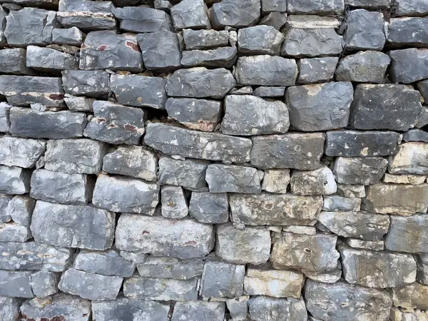 Düz olmayan dikdörtgen taşlar ve havan hatları içeren taştan bir duvar dokusu..