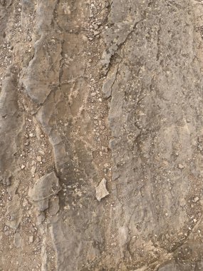 Dağılmış çakıl taşlı sert kahverengi kayaların yakın çekimi doğal çatlaklar ve dokular sergiliyor. Arkaplan, tasarım veya mimari referanslar için mükemmel.
