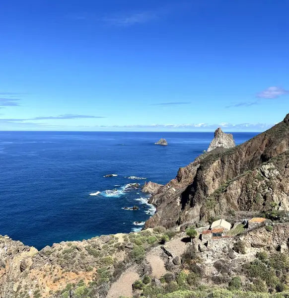 İspanya 'nın Kanarya Adaları, Tenerife' nin kuzey kıyısındaki dik volkanik kayalıklar. Uzak bir kırsal yerleşim alanı engebeli kıyı şeridinin kenarında, derin mavi Atlantik Okyanusu ufka doğru uzanıyor..