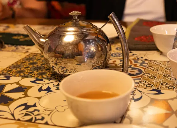 Gümüş çaydanlık ve çay fincanları desenli masada.