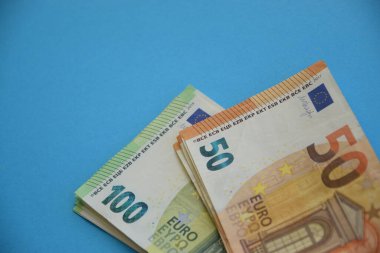 Açık mavi kağıt arka planda 100 ve 50 Euro 'luk banknotlar kapanıyor.