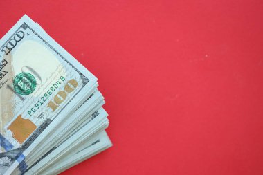 Büyük miktarlarda 100 dolarlık banknotlar parlak kırmızı kağıtların üzerinde duruyor.