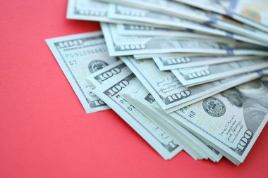 Büyük miktarlarda 100 dolarlık banknotlar parlak kırmızı kağıtların üzerinde duruyor.