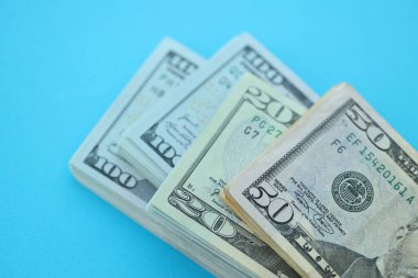 Büyük miktarda yüz, elli ve yirmi dolarlık banknotlar parlak mavi renkli kağıtların üzerinde uzanır.