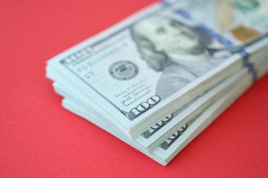 Büyük miktarlarda 100 dolarlık banknotlar parlak kırmızı kağıtların üzerinde duruyor.