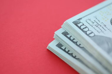 Büyük miktarlarda 100 dolarlık banknotlar parlak kırmızı kağıtların üzerinde duruyor.