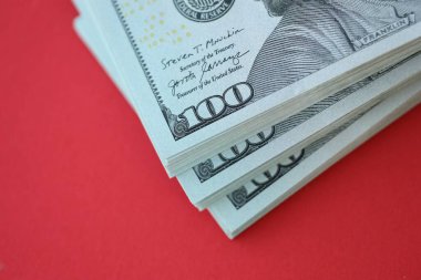 Büyük miktarlarda 100 dolarlık banknotlar parlak kırmızı kağıtların üzerinde duruyor.
