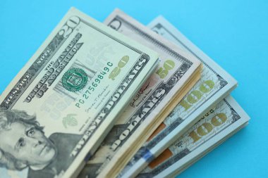 Büyük miktarda yüz, elli ve yirmi dolarlık banknotlar parlak mavi renkli kağıtların üzerinde uzanır.