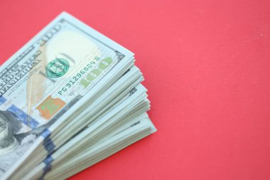Büyük miktarlarda 100 dolarlık banknotlar parlak kırmızı kağıtların üzerinde duruyor.