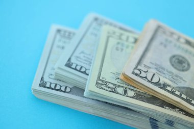 Büyük miktarda yüz, elli ve yirmi dolarlık banknotlar parlak mavi renkli kağıtların üzerinde uzanır.