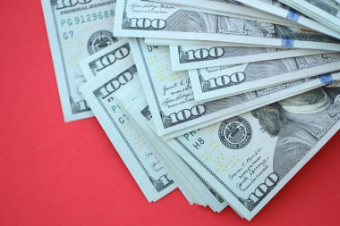 Büyük miktarlarda 100 dolarlık banknotlar parlak kırmızı kağıtların üzerinde duruyor.