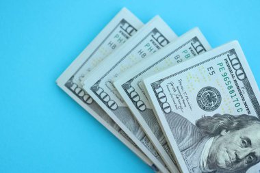 Büyük miktarlarda 100 dolarlık banknotlar parlak mavi renkli kağıtların üzerinde uzanır.