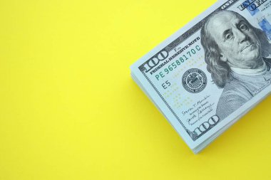 Büyük miktarlarda 100 dolarlık banknotlar parlak sarı renkli kağıtların üzerinde uzanır.
