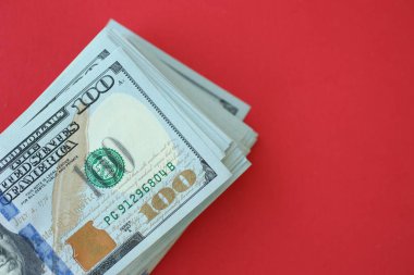 Büyük miktarlarda 100 dolarlık banknotlar parlak kırmızı kağıtların üzerinde duruyor.