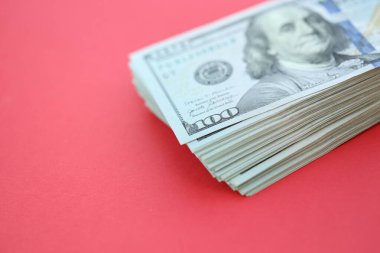 Büyük miktarlarda 100 dolarlık banknotlar parlak kırmızı kağıtların üzerinde duruyor.