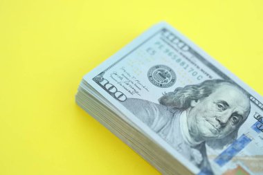 Büyük miktarlarda 100 dolarlık banknotlar parlak sarı renkli kağıtların üzerinde uzanır.