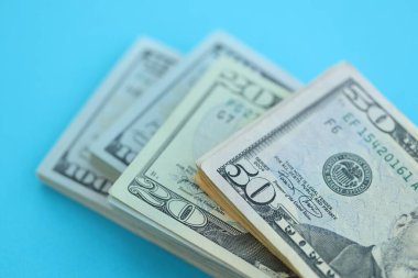 Büyük miktarda yüz, elli ve yirmi dolarlık banknotlar parlak mavi renkli kağıtların üzerinde uzanır.
