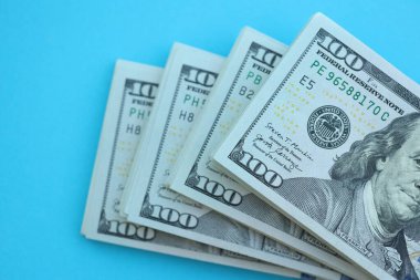 Büyük miktarlarda 100 dolarlık banknotlar parlak mavi renkli kağıtların üzerinde uzanır.