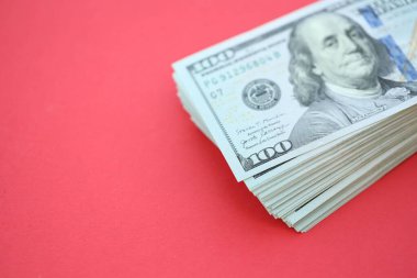Büyük miktarlarda 100 dolarlık banknotlar parlak kırmızı kağıtların üzerinde duruyor.