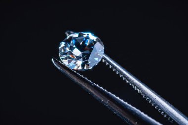 Metal kuyumcu cımbızında tutulan elmas seçici odaklı, yakın mesafeden kesilmiş parlak taş. Profesyonel fotoğraf.