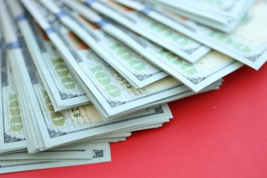 Büyük miktarlarda 100 dolarlık banknotlar parlak kırmızı kağıtların üzerinde duruyor.